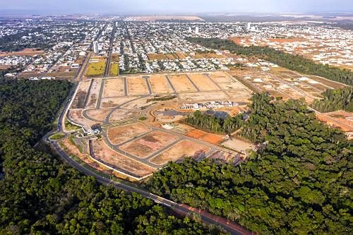 Vista aérea de loteamento em implantação, com vias e infraestrutura abertas e a cidade consolidada ao fundo